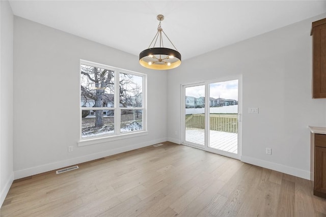 unfurnished dining area featuring light wood-type flooring and a notable chandelier