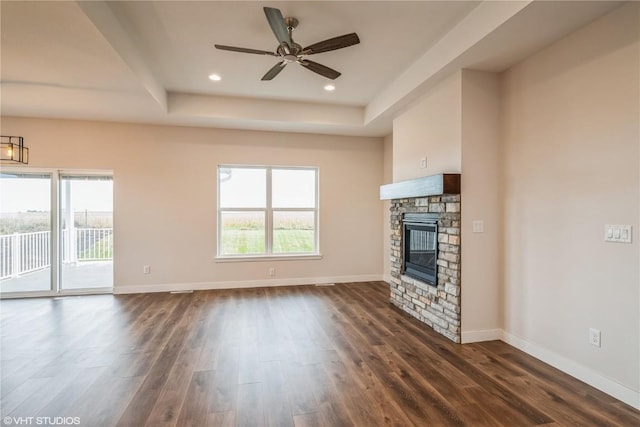 unfurnished living room with a tray ceiling, a stone fireplace, and a healthy amount of sunlight