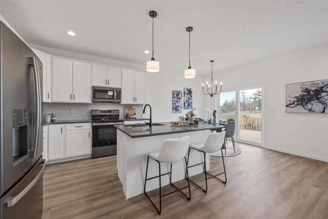 kitchen featuring a kitchen island with sink, light hardwood / wood-style flooring, stainless steel appliances, pendant lighting, and white cabinets