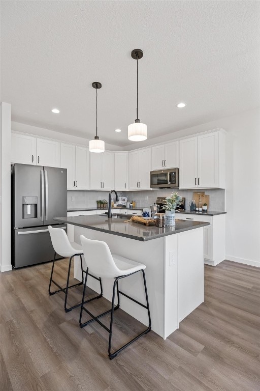 kitchen with appliances with stainless steel finishes, light hardwood / wood-style flooring, a center island with sink, and white cabinets