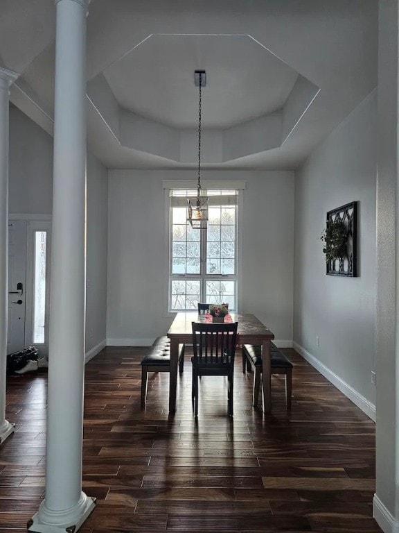 dining room featuring decorative columns, dark hardwood / wood-style flooring, a tray ceiling, and a notable chandelier