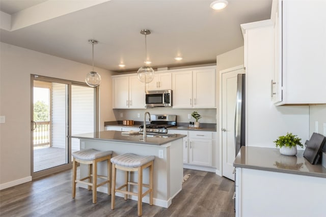 kitchen with an island with sink, stainless steel appliances, dark hardwood / wood-style flooring, and white cabinets