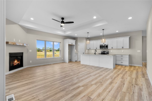 kitchen featuring light hardwood / wood-style flooring, white cabinets, a center island with sink, ceiling fan, and a raised ceiling