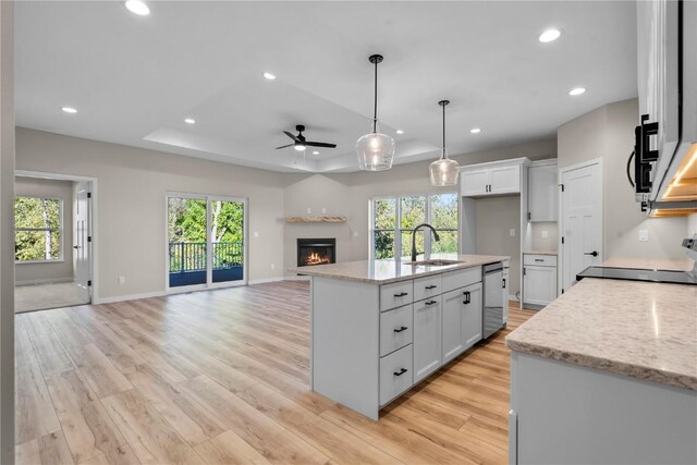 kitchen with sink, light stone counters, light wood-type flooring, white cabinetry, and ceiling fan