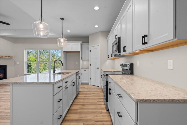 kitchen featuring light wood-type flooring, an island with sink, appliances with stainless steel finishes, decorative light fixtures, and sink