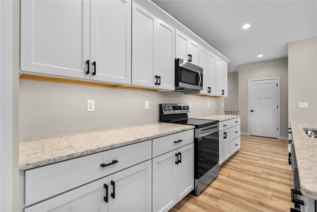 kitchen with white cabinets, stainless steel appliances, light stone countertops, and light wood-type flooring