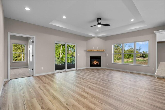 unfurnished living room with light hardwood / wood-style floors, a raised ceiling, and plenty of natural light