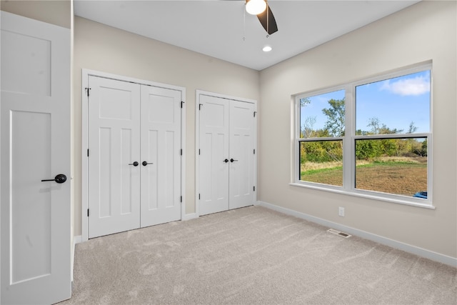 unfurnished bedroom featuring multiple closets, ceiling fan, and light colored carpet