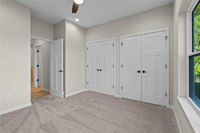 unfurnished bedroom featuring two closets, multiple windows, light colored carpet, and ceiling fan