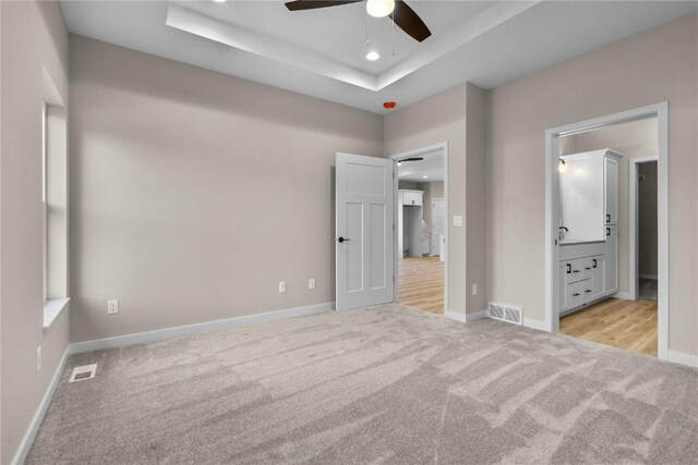 unfurnished bedroom featuring a tray ceiling, light hardwood / wood-style floors, and ceiling fan