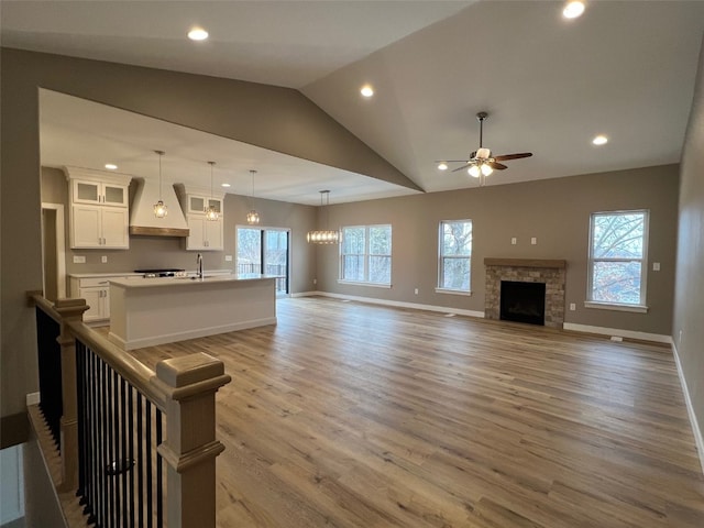 living room with lofted ceiling, ceiling fan with notable chandelier, sink, hardwood / wood-style flooring, and a fireplace