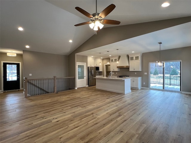 unfurnished living room with ceiling fan with notable chandelier, a healthy amount of sunlight, light hardwood / wood-style floors, and vaulted ceiling