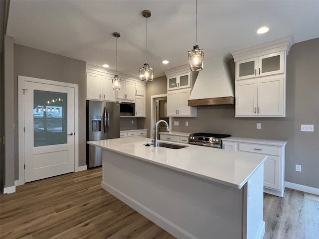 kitchen featuring premium range hood, dark wood-type flooring, a center island with sink, sink, and appliances with stainless steel finishes