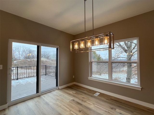 unfurnished dining area featuring a wealth of natural light, wood-type flooring, and an inviting chandelier