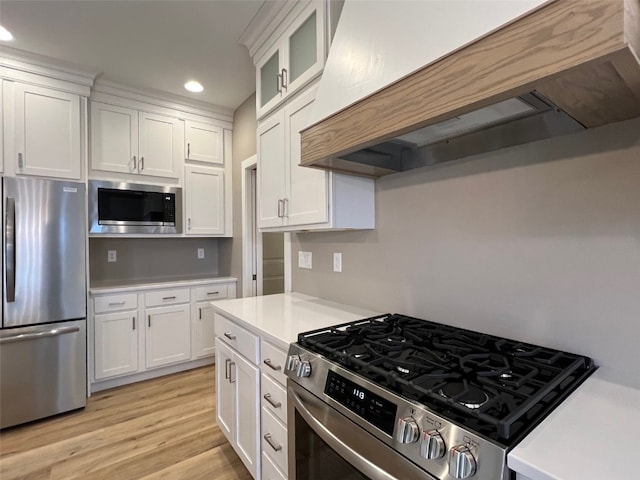 kitchen with appliances with stainless steel finishes, light wood-type flooring, white cabinetry, and custom range hood