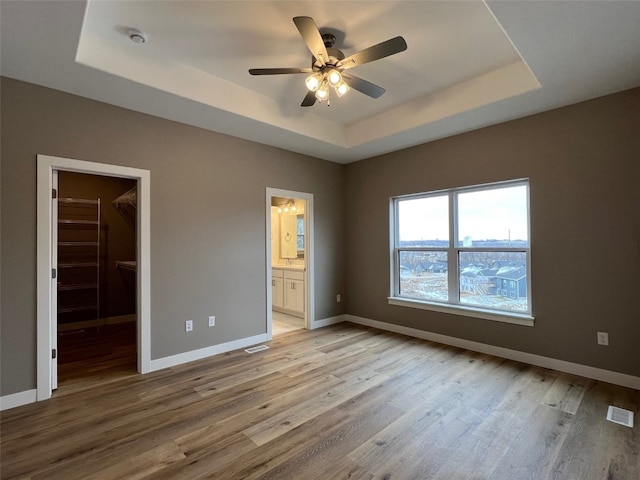 unfurnished bedroom featuring a raised ceiling, a walk in closet, light hardwood / wood-style flooring, and ensuite bath