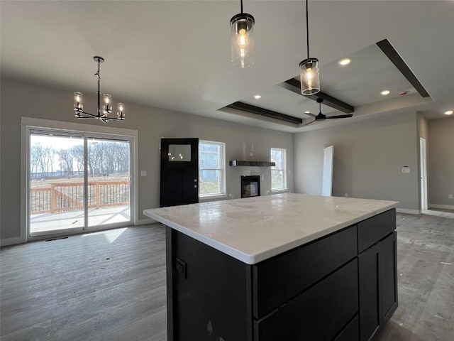 kitchen with pendant lighting, light hardwood / wood-style flooring, a center island, and a raised ceiling