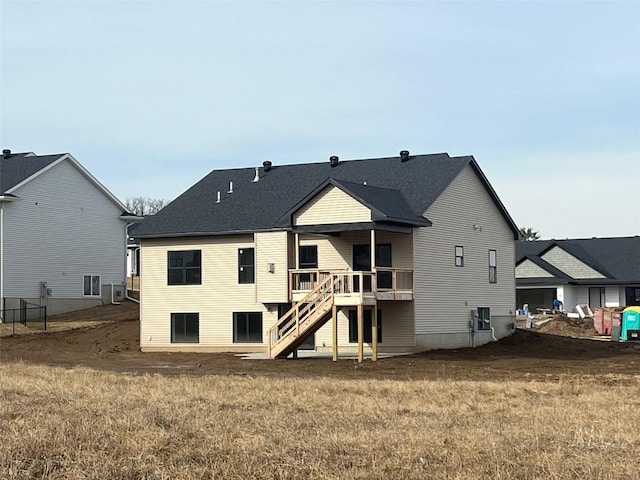 rear view of house featuring roof with shingles, stairway, a deck, and a yard