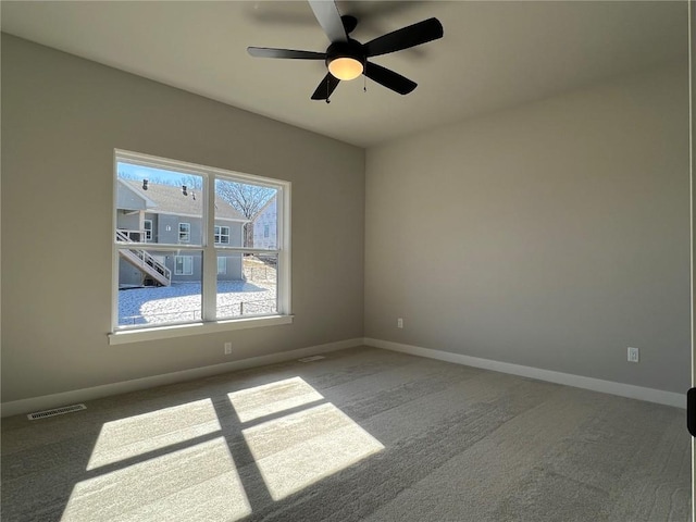 carpeted spare room featuring a ceiling fan, visible vents, and baseboards