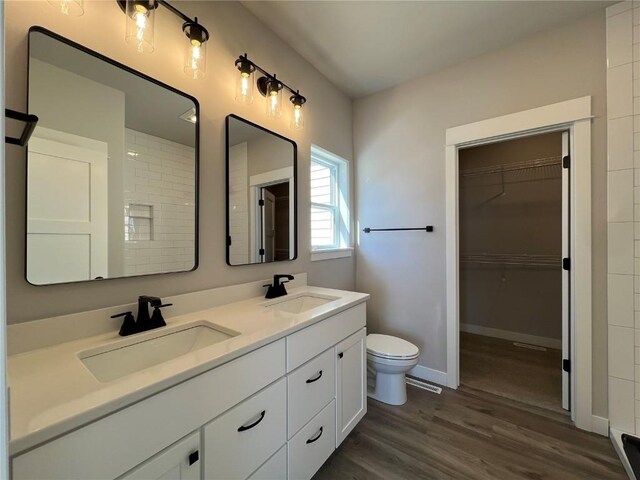 bathroom featuring double vanity, wood finished floors, a sink, and toilet