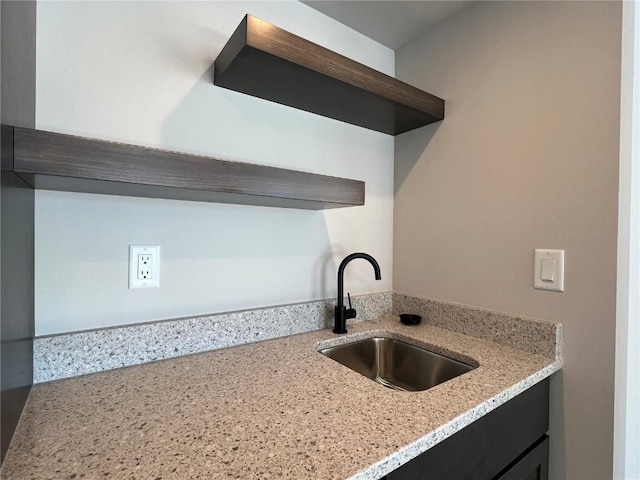 kitchen featuring open shelves, light stone counters, a sink, and dark cabinetry