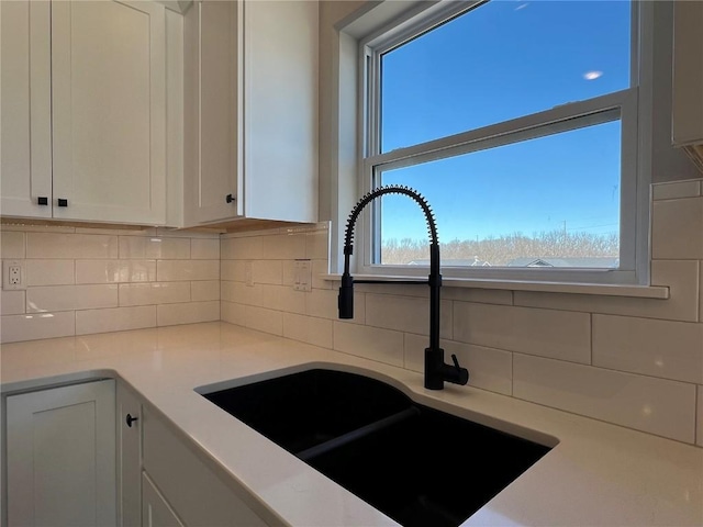 kitchen featuring backsplash, white cabinets, a sink, and light countertops