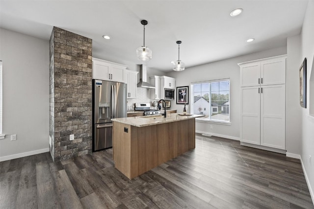 kitchen featuring decorative light fixtures, a kitchen island with sink, wall chimney range hood, white cabinetry, and stainless steel appliances