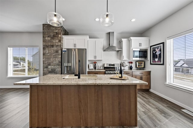 kitchen with wall chimney exhaust hood, white cabinetry, light stone countertops, and a healthy amount of sunlight