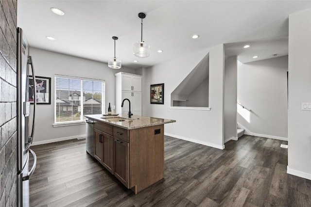 kitchen with light stone counters, sink, a center island with sink, decorative light fixtures, and dark hardwood / wood-style floors