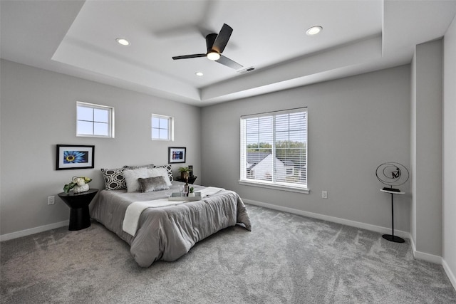 carpeted bedroom with ceiling fan and a raised ceiling