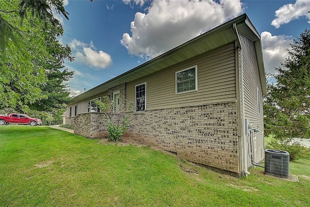 view of side of property featuring a yard, brick siding, and central AC