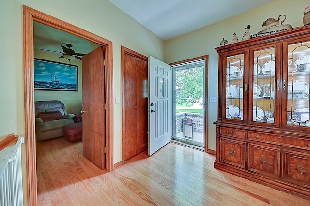 foyer entrance featuring baseboards, light wood-style floors, a ceiling fan, and radiator heating unit