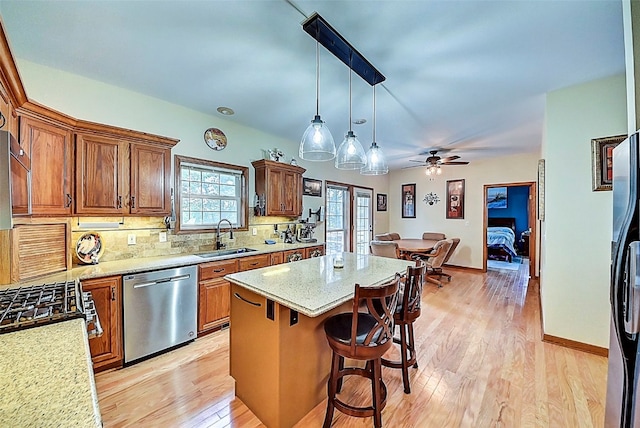 kitchen with light wood finished floors, a breakfast bar, a sink, stainless steel dishwasher, and a center island