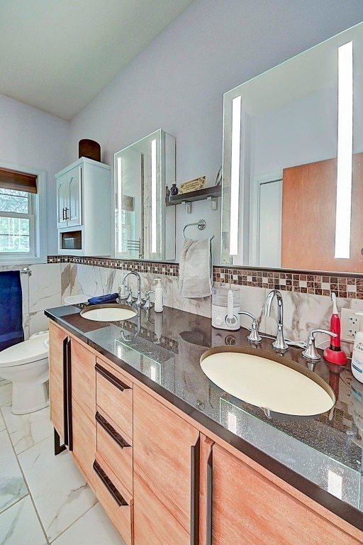 bathroom featuring a sink, toilet, marble finish floor, and double vanity