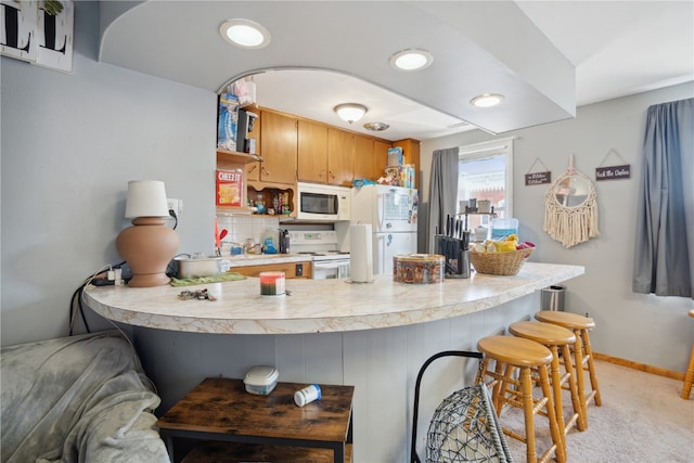 kitchen featuring decorative backsplash, a kitchen bar, kitchen peninsula, white appliances, and light carpet