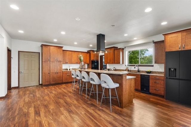 kitchen featuring a center island, a kitchen breakfast bar, brown cabinets, black appliances, and island exhaust hood