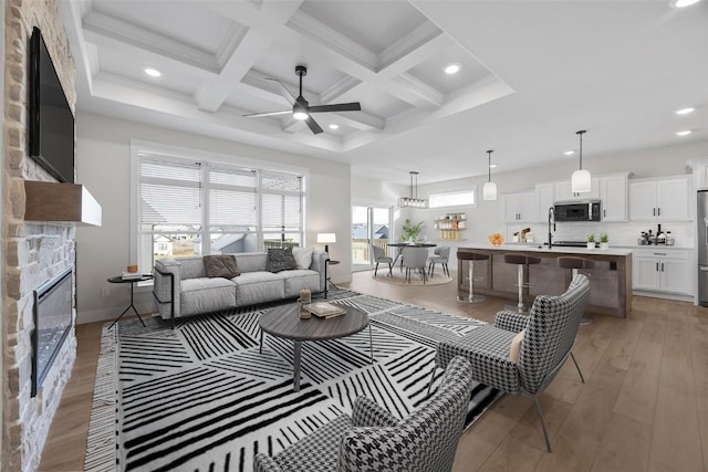 living room with ceiling fan, coffered ceiling, beamed ceiling, light hardwood / wood-style floors, and a fireplace