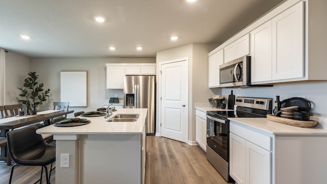 kitchen with light hardwood / wood-style flooring, appliances with stainless steel finishes, white cabinetry, sink, and a center island with sink