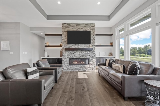 living room featuring a fireplace, a tray ceiling, dark wood finished floors, and recessed lighting