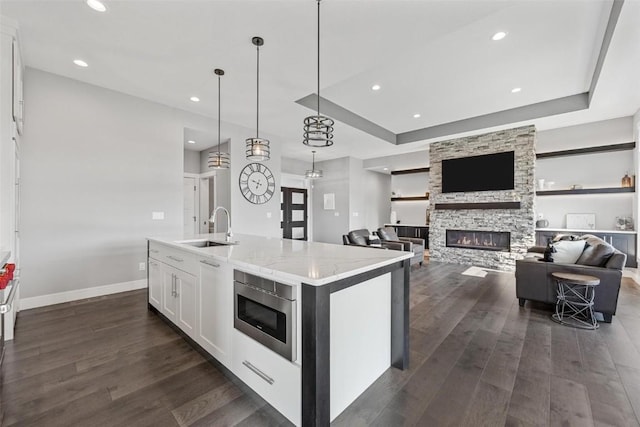 kitchen featuring light stone counters, a sink, white cabinets, a center island with sink, and pendant lighting