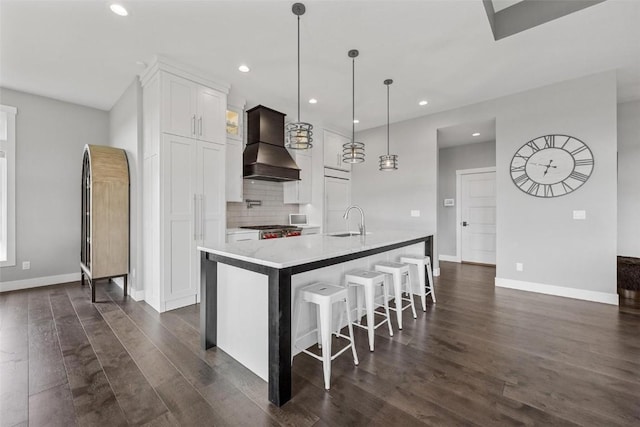 kitchen with white cabinets, an island with sink, decorative light fixtures, custom exhaust hood, and light countertops