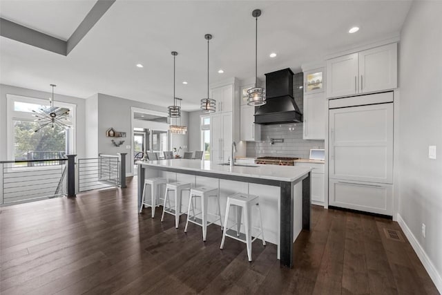 kitchen featuring a center island with sink, light countertops, hanging light fixtures, white cabinets, and premium range hood