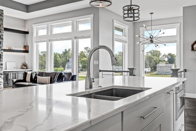 kitchen with light stone counters, pendant lighting, a notable chandelier, and a sink