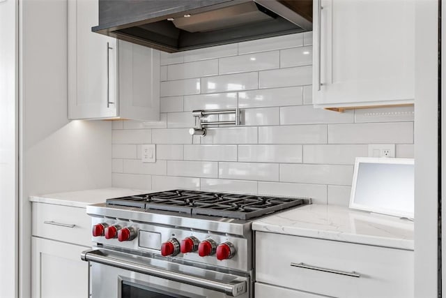 kitchen with light stone countertops, white cabinets, wall chimney range hood, high end stainless steel range, and decorative backsplash