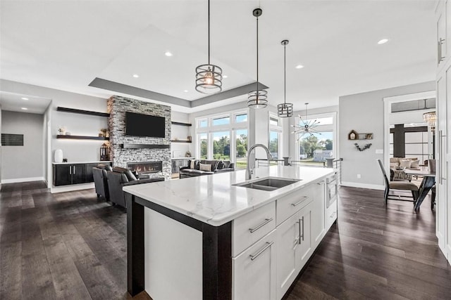 kitchen featuring light stone counters, white cabinets, a sink, and an island with sink