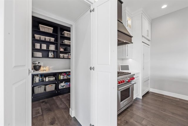 kitchen with wall chimney exhaust hood, high end range, dark wood-style flooring, light countertops, and white cabinetry