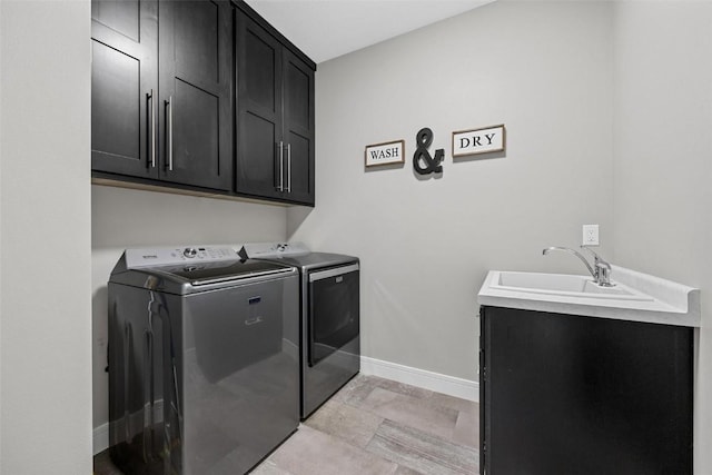 washroom featuring a sink, washing machine and dryer, cabinet space, and baseboards