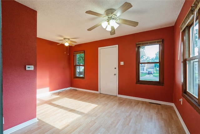 empty room featuring a wealth of natural light, ceiling fan, and light hardwood / wood-style floors