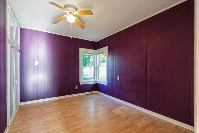 unfurnished room with light wood-type flooring, wood walls, ceiling fan, and crown molding