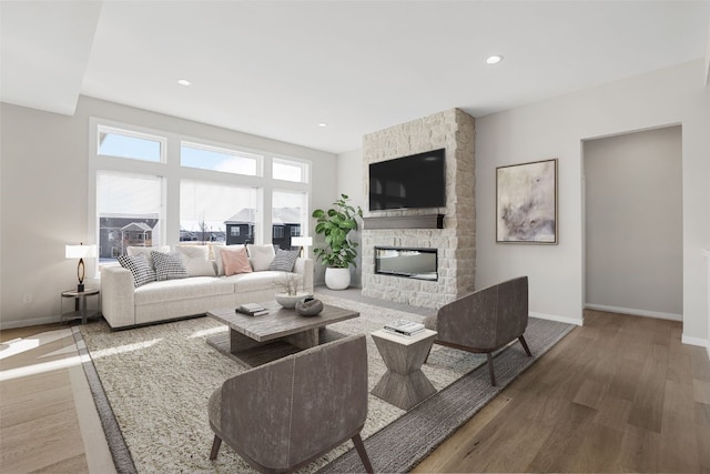 living area with recessed lighting, a stone fireplace, baseboards, and wood finished floors